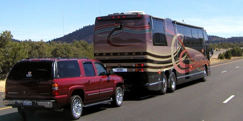 Large Motorhome in mountains flat towing a red Chevrolet Suburban