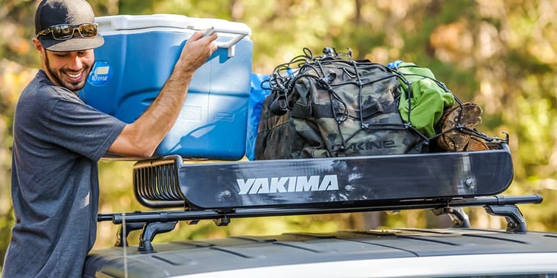 Man loading blue cooler into roof top yakima cargo rack