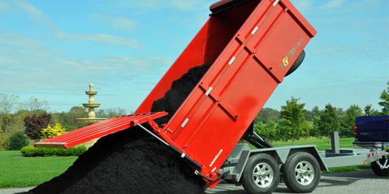 Truck towing red B-wise dump trailer full of black soil